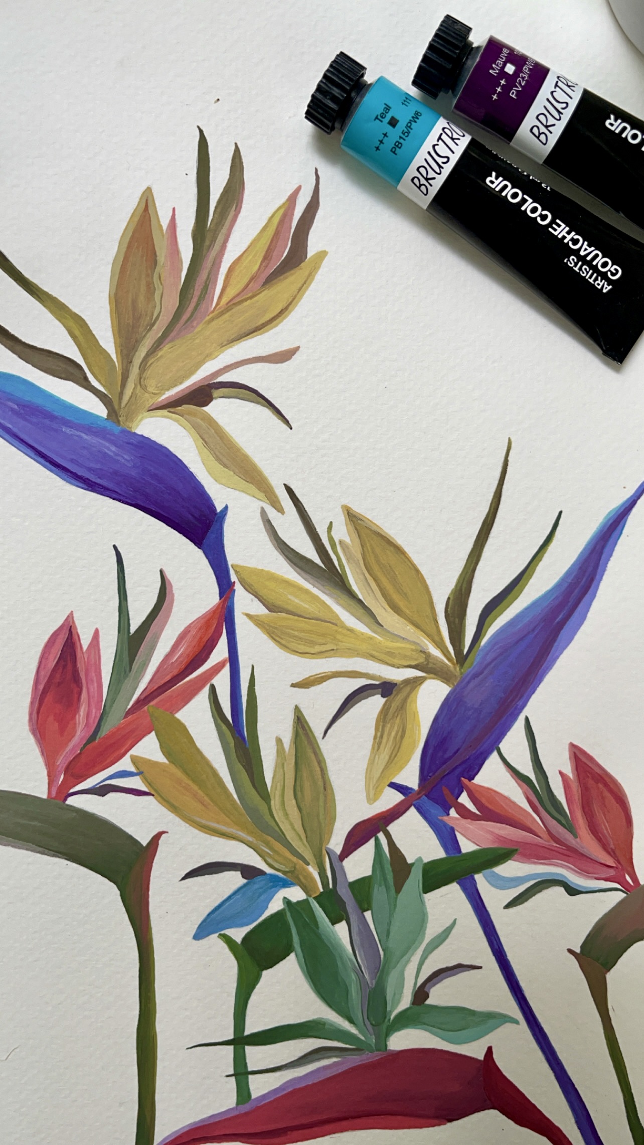 Gouache painting in progress of bird-of-paradise flowers in purple, yellow and red, with paint tubes resting on the page